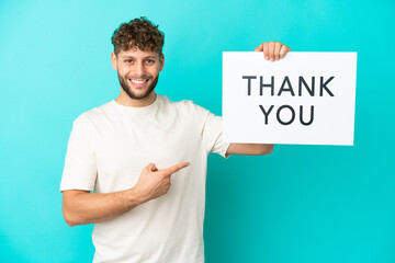 Wall Mural - Young handsome caucasian man isolated on blue background holding a placard with text THANK YOU and  pointing it