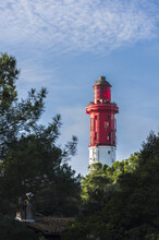 Cap Ferret's Red And White Lighthouse Hidden Behind A Pine Tree Forest During A Sunny Day