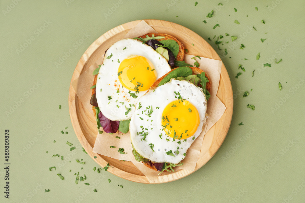 Delicious sandwiches with fried eggs on green background