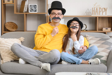 Poster - Portrait of father and his little daughter with paper mustache sitting on sofa at home