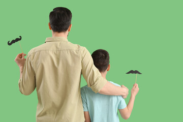 Sticker - Father and his little son with paper mustache hugging on green background, back view