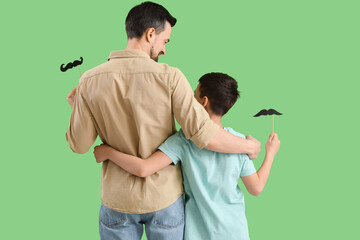 Poster - Father and his little son with paper mustache hugging on green background, back view