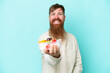 © luismolinero - Redhead man with long beard holding a bowl of fruit isolated on blue background with happy expression
