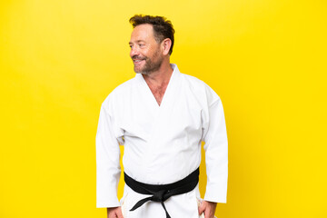 middle age caucasian man doing karate isolated on yellow background looking side