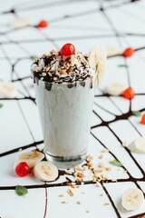 Poster - Closeup shot of a tall glass cup of milkshake topped with whipped cream, crushed nuts and a cherry