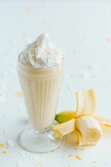 Wall Mural - Closeup shot of a tall glass cup of banana milkshake topped with whipped next to banana