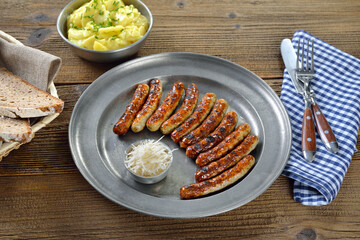 Zehn gebratene Nürnberger Röstbratwürstchen mit frischem Meerrettich auf einem Zinnteller, dazu Kartoffelsalat  -Ten fried Nuremberg sausages with horseradish served on a pewter plate with a bowl of p