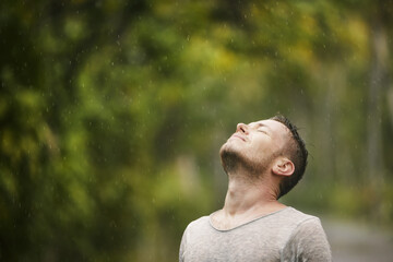 Portrait of man in wet clothes with eyes closed enjoying heavy rain in nature. Themes of life water, weather and environment..