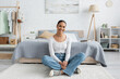 cheerful african american student in jeans sitting with crossed legs near bed at home.