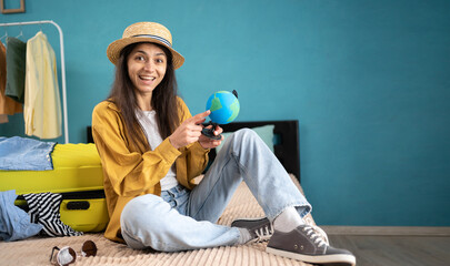 Happy woman planning holiday trip. Cheerful lady in hat choosing her dream destination on Earth globe. Traveling and active vacation concept