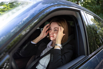 Wall Mural - Young attractive businesswoman in suit driving and standing in a traffic jam. Tired business lady sitting in car and feeling bad because of long time of traffic light