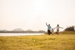 © Kiattisak - Happy Family enjoying a peaceful walk and running in a scenic field with a serene lake in the background.