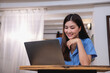 © PHAISITSAWAN - Asian woman with a beautiful smile and face sits comfortably on her desk at home with a laptop and notebook for relaxing and relaxing in a bright morning. holiday vacation concept.