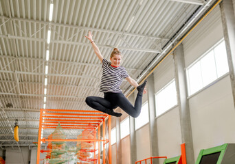 Poster - Pretty girl in trampoline park jumping and making split pose in air. Happy teenager enjoying amusement activities and stretching