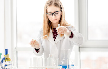 Smart girl during scientific chemistry experiment wearing protection glasses, holding tubes and measuring ingridients. Schoolgirl with chemical equipment on school lesson