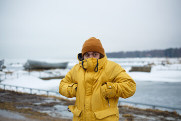 man with beard in yellow winter jacket with hood and brown hat hid his nose and face in collar. cold