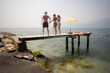 © BerndRolauffs - Family on vacation holding hands and jumping off a jetty of picturesque Lake Garda in Italy