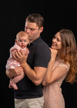 a young family with a baby in their arms. dad kisses the newborn, mom looks tenderly. the girl is dr