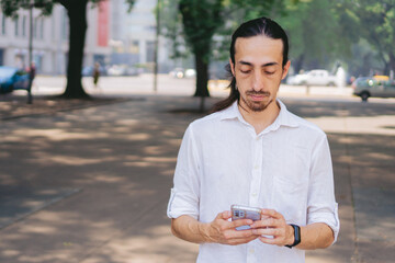 young latin man with long hair and shirt in an urban environment checking his cell phone. copy space