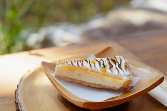 traditional lemon cheesecake tart slice with lemon curd meringue on wooden dish and table. delicious