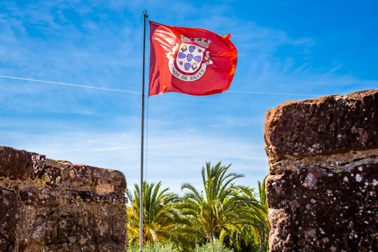 red flag with coat of arms of cidade de silves waves in the wind against the backdrop of blue sky an