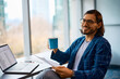 © Drazen - Happy entrepreneur having cup of coffee while working in office and looking at camera.
