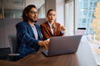 © Drazen - Young businessman talks to female colleague while working on computer in office.