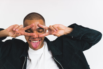 Wall Mural - Positive funny male student posing with his tongue out and showing v sign with two hands in front of his face. Isolated over white background. High quality photo