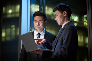 two asian businessmen discussing business in office using laptop computer