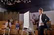 © Roman - Male speaker giving presentation to students in hall at university.conference hall. Participants sit listening while speaker is writing on board. Scientific, business event, training. Education