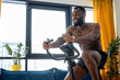 © Roman - Young black fitness man training on a stationary bike, exercise at home alone. handsome male riding stationary bike or exercise bike, working out and doing exercise for legs in the morning