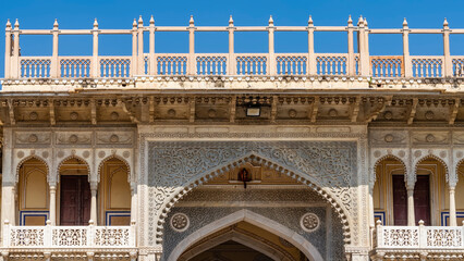 Wall Mural - Details of the architecture of the ancient City Palace in Jaipur. Elegant arched entrance, galleries with columns and openwork lattice. Railings along the edge of the roof against the blue sky. India.