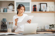 © interstid - Happy Asian woman using laptop for working at home in kitchen