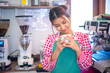 © Digital Art Studio - Beautiful asian barista staff wearing an apron looking at her cup of coffee meticulously brewed with smile.