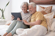 © luciano - Portrait of happy senior couple together in bed, handsome people relaxing at home using digital tablet technology, leisure time