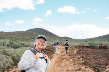 Sticker - Happy senior woman with hat and eyeglasses in a trekking day in country footpath, enjoying healthy lifestyle and freedom, vacation or retirement concept