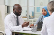 © AnnaStills - African American professional doctor in white coat discussing the way of treatment together with his colleagues during meeting in office
