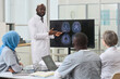 © AnnaStills - African American doctor in white coat presenting x-ray image on monitor to his colleagues during medical conference