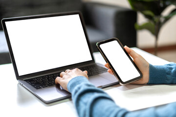 Woman working with smartphone and modern laptop computer blank white desktop screen for advertising, mockup, technology, advertising, search information, creative design on table