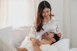 © PHAISITSAWAN - Happy young asian couple embracing, teasing, playing cheerfully in bed at home, romantic time to enhance family bonding. family concept.