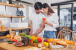 © PHAISITSAWAN - Young Asian couple cooking with fruits and vegetables and using laptop in the kitchen To cook food together within the family happily, family concept.