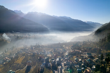  aerial drone shot gaining height over fog covered valley town of manali hill station with himalaya range in distance showing this popular tourist destination