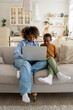 © DimaBerlin - Happy African American family mother and little kid son watching cartoons on laptop together, sitting on couch at home. Sleeping mom and child looking at computer screen having video call