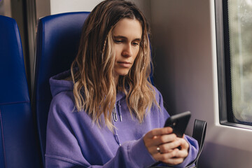 Wall Mural - Modern people city lifestyle. Young urban blonde woman using phone app, chatting, scrolling social media pages. Girl enjoying train travel in business class seat. Transport travel lifestyle.