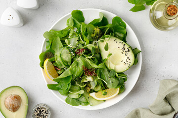 Healthy green salad with lettuce, avocado and microgreens. Vegetarian meal in a bowl, fresh diet dinner salad on the plate and grey background.