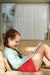 © DragonImages - Smiling preteen girl sitting on sofa and doing homework