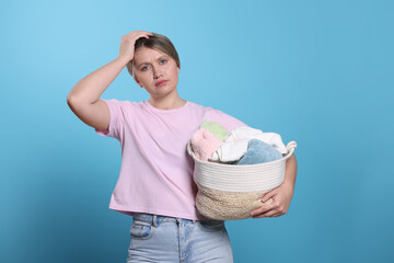 Wall Mural - Tired woman with basket full of laundry on light blue background