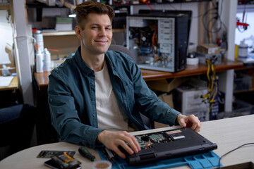 Wall Mural - professional young repairman or technician repairs computers and laptop. portrait of service engineer in shirt repairing a laptop, happy guy looking at camera, posing, successful job