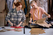 © Roman - two young caucasian hardworking seamstresses in modern studio workshop, preparing textile to sew, redhead and blonde ladies in casual wear in fabric, having talk, clothing manufactory production