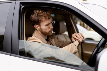 Serious man in casual clothes sitting in car, looking at his watch, checking time. Successful businessman, business concept